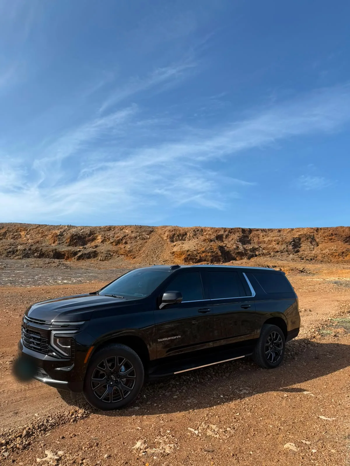 A black Chevrolet Suburban parked on red desert ground under a blue sky in Aruba