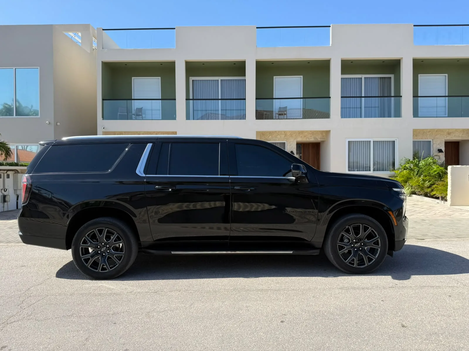 A black Chevrolet Suburban parked on a quiet street in front of modern townhouses in Aruba